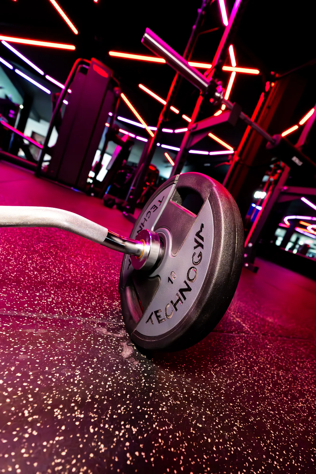 Technogym barbell plate on the studio floor under pink neon at ONE PULS Brussels