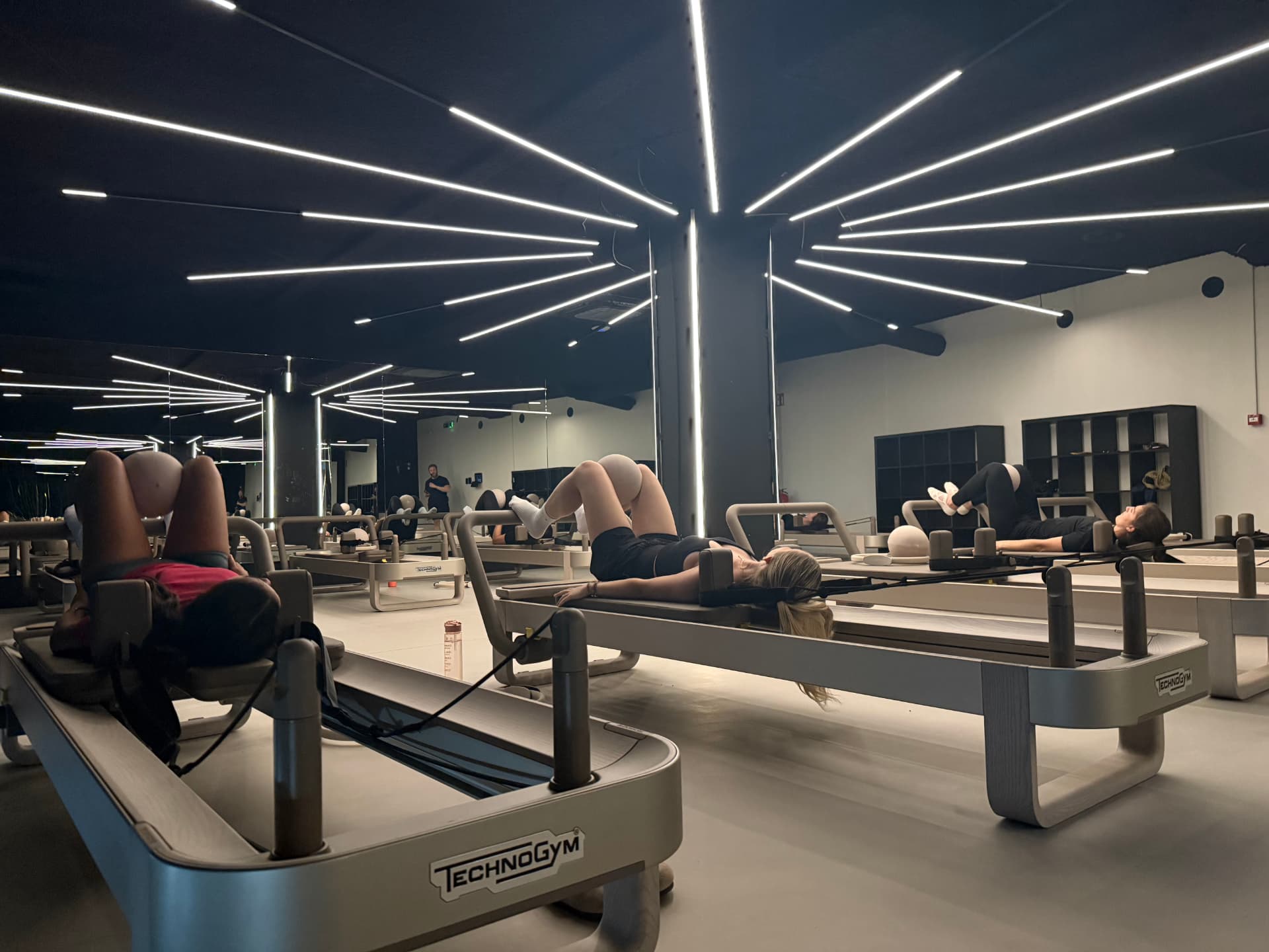 Reformer Pilates class on Technogym reformers under linear neon lighting at ONE PULS Brussels
